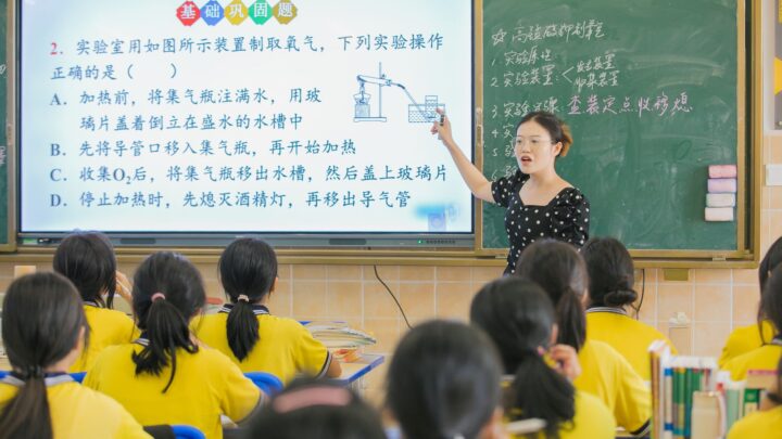 A teacher instructs students in a chemistry class, using a digital board for interactive learning.