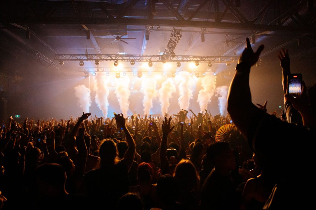 Energetic crowd enjoying a concert with dynamic lighting and smoke effects in an indoor venue. 文章配图