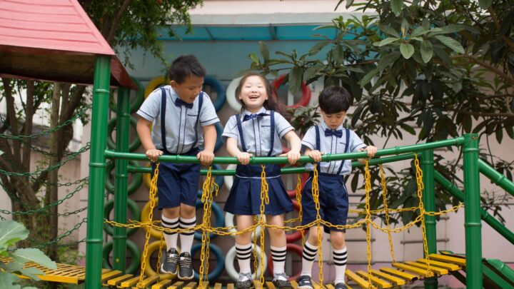 Three children in school uniforms enjoy playing on a vibrant playground bridge.