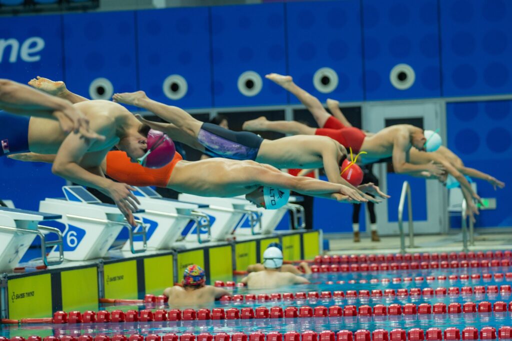 Group of athletes diving into a swimming pool during a competition, showcasing synchronized starting technique.