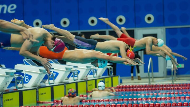 Group of athletes diving into a swimming pool during a competition, showcasing synchronized starting technique.