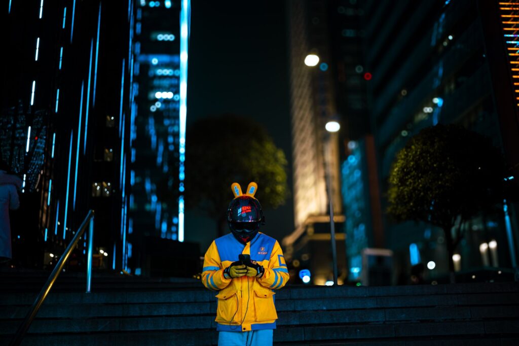A delivery rider stands amidst the vibrant neon cityscape of Chongqing, China at night.