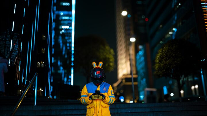A delivery rider stands amidst the vibrant neon cityscape of Chongqing, China at night.