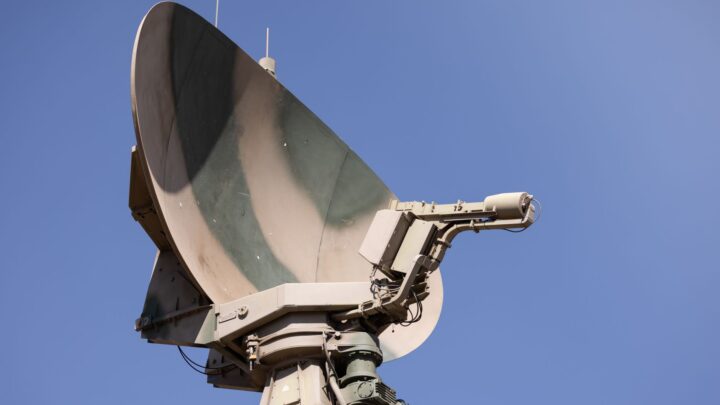 Close-up of a military radar system with a clear blue sky as background, showcasing advanced communication technology.