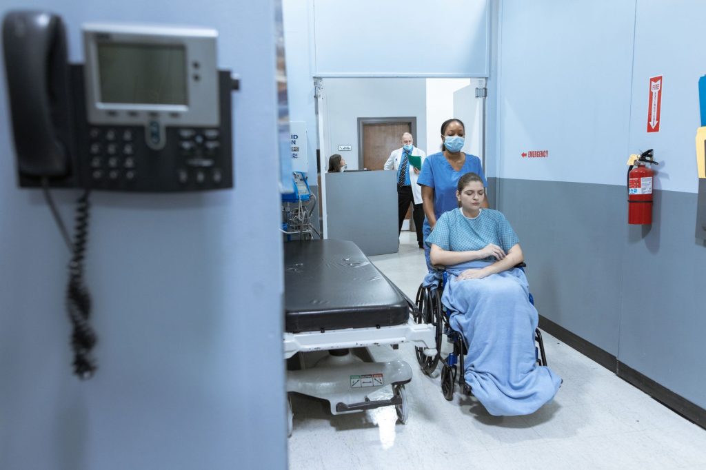 A nurse helps a patient in a wheelchair down a hospital corridor, reflecting care and medical professionalism. 文章配图