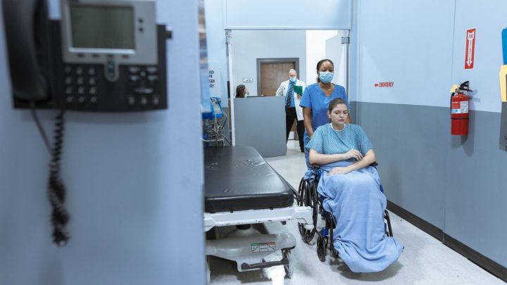 A nurse helps a patient in a wheelchair down a hospital corridor, reflecting care and medical professionalism. 文章配图