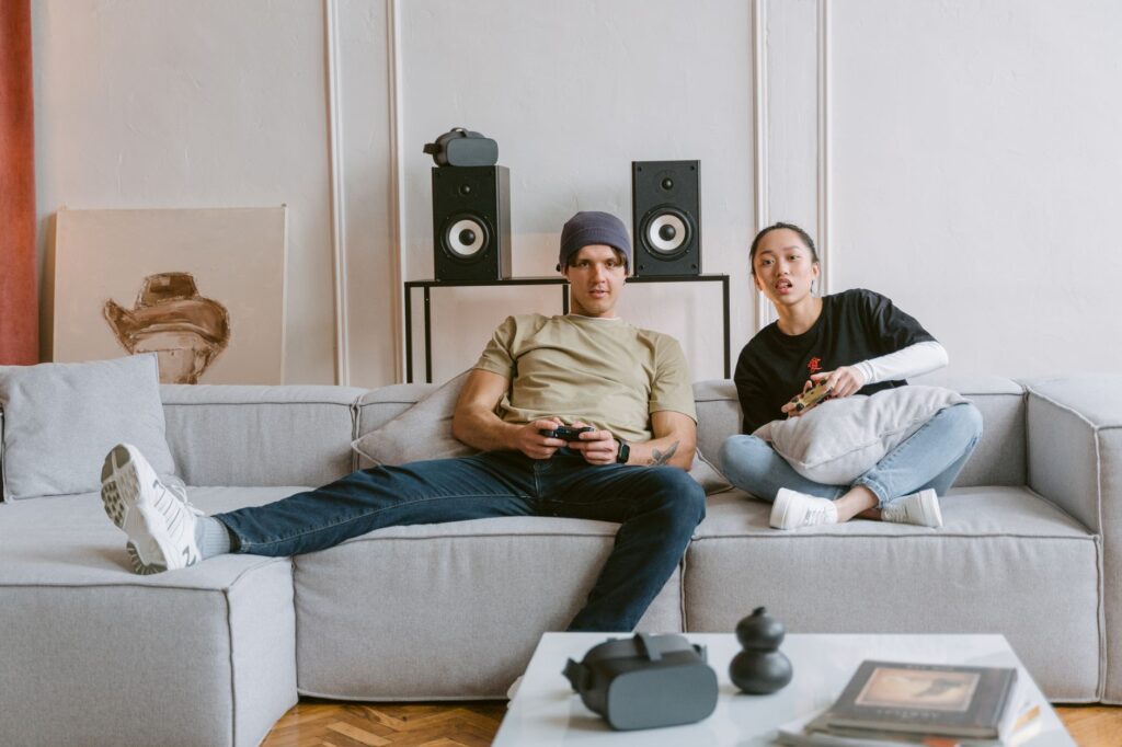 A young couple relaxes on a couch playing video games, enjoying leisure time indoors.