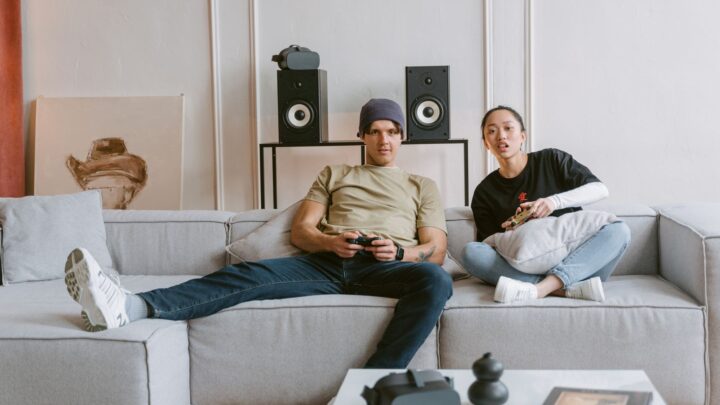 A young couple relaxes on a couch playing video games, enjoying leisure time indoors.