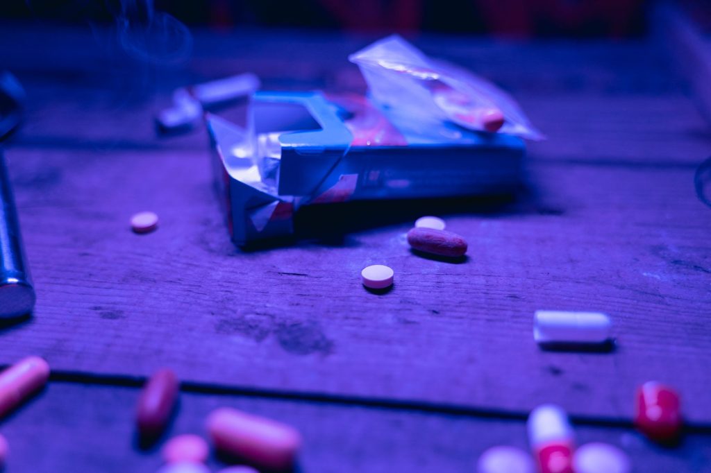 Various pills scattered on a wooden table under purple light, depicting medication or substance concept. 文章配图