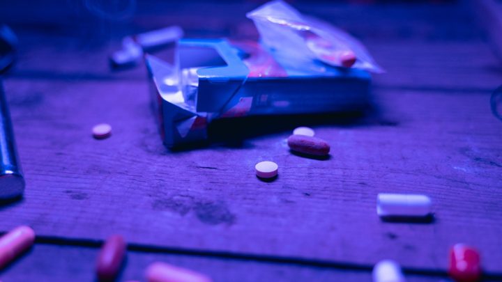 Various pills scattered on a wooden table under purple light, depicting medication or substance concept. 文章配图