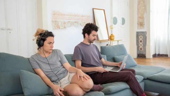 A couple relaxing on a sofa with headphones and laptop, creating a cozy home atmosphere.