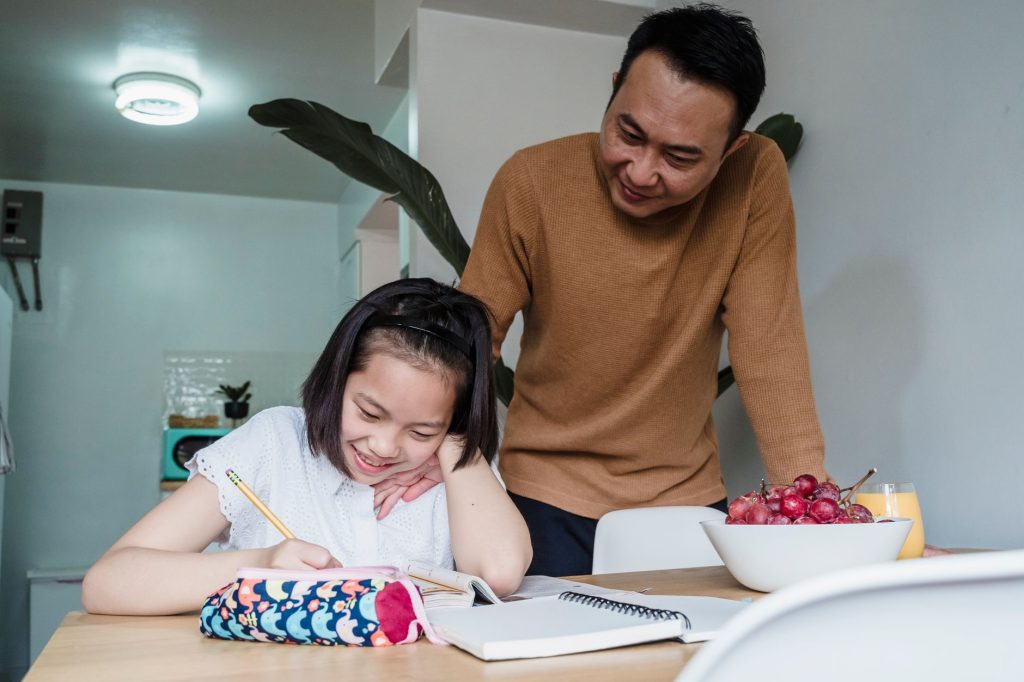 parent helping child with homework at dining table evening warm lighting