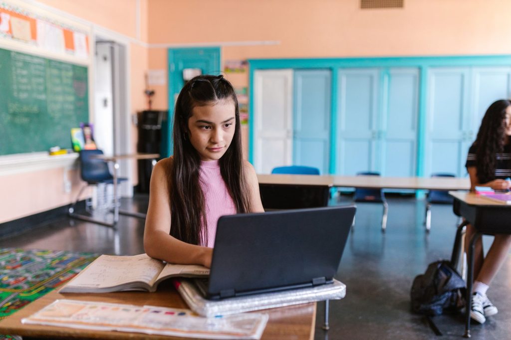 middle school student studying independently at desk with notebook and laptop