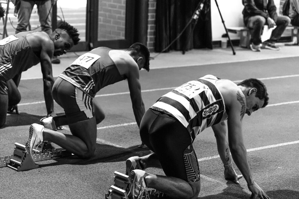 Three athletes in starting blocks ready for an indoor track race, showcasing focus and determination.