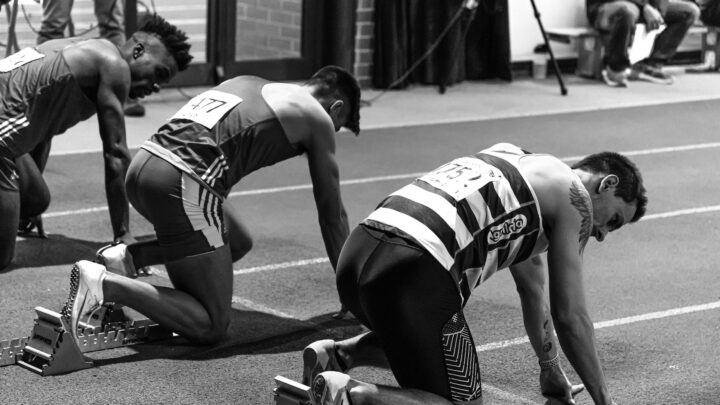 Three athletes in starting blocks ready for an indoor track race, showcasing focus and determination.