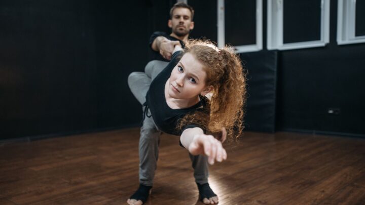 Two dancers perform a captivating move in a dance studio, showcasing their flexibility and strength.