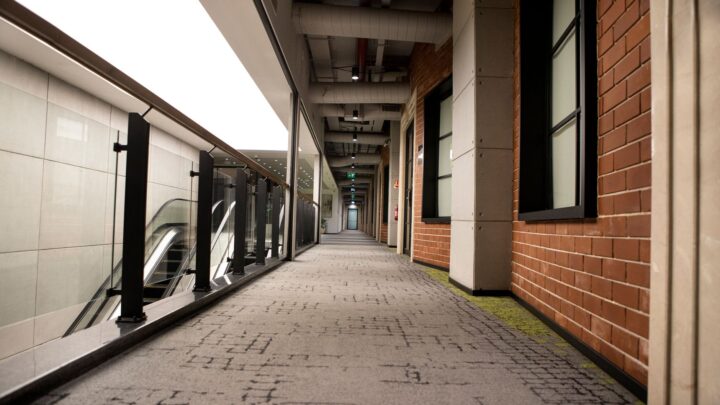 A modern indoor hallway featuring brick walls and carpet flooring, with escalators and handrails.
